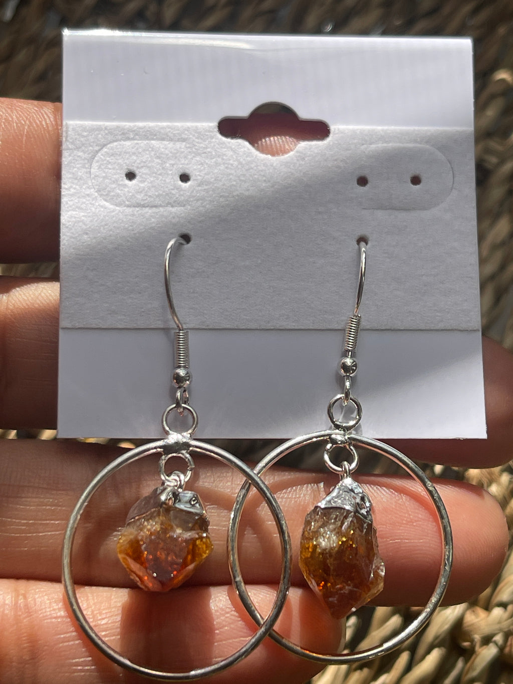Citrine Point Circle Earrings, Silver hoop earrings with amber-colored stones held over a white card.