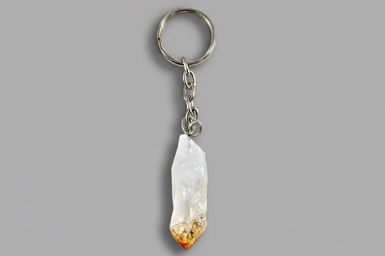 A metal keychain with a loop attachment and a polished citrine crystal point dangled from it against a gray background.