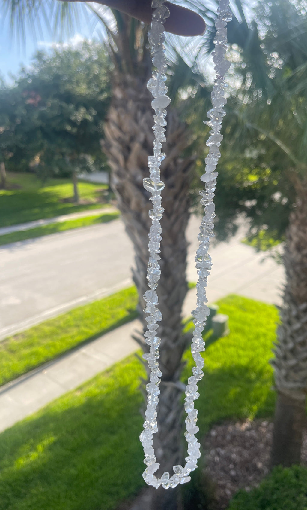 Close-up of a Clear_Quartz_Necklace_30-32_Inches with palm trees and a road in the background