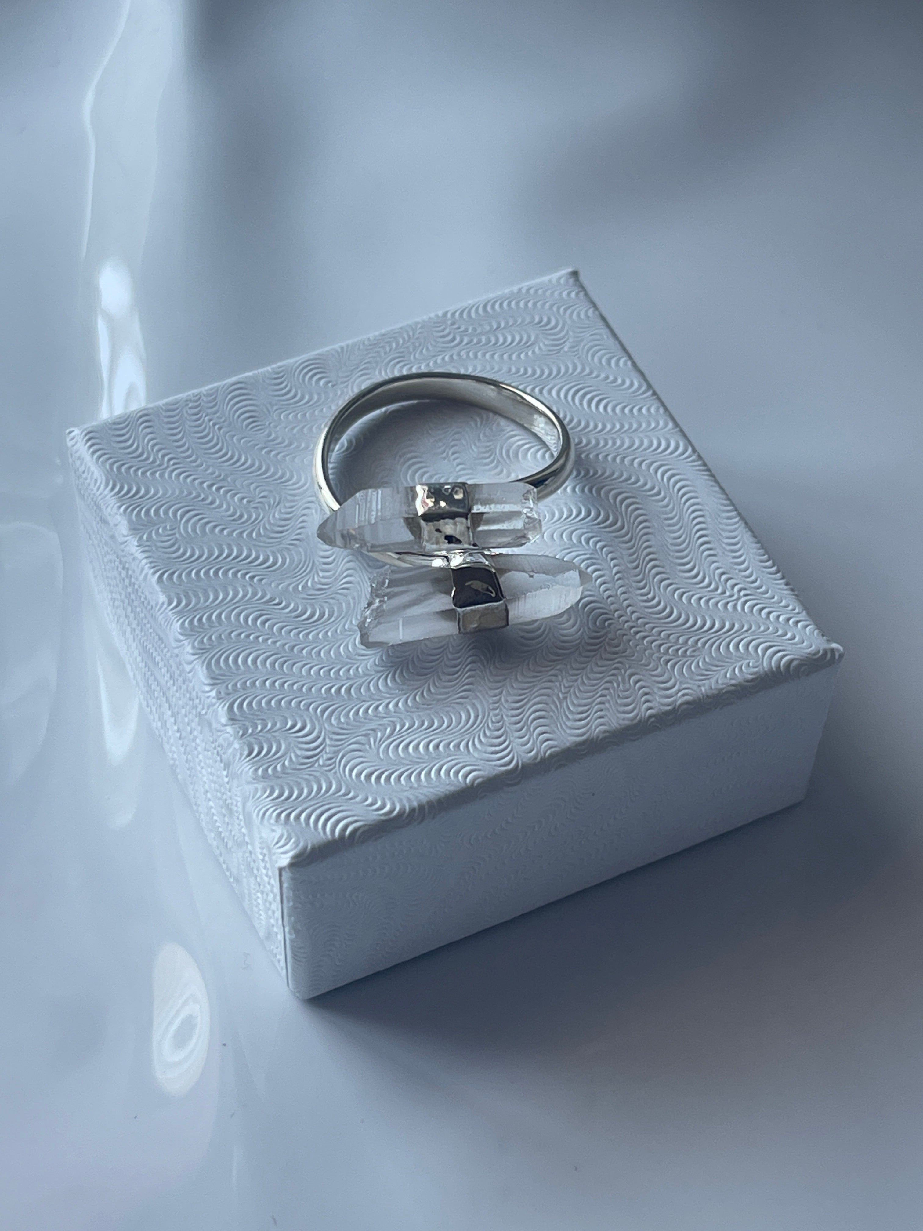 Silver clear quartz ring with a clear stone on a textured white box against a white  background