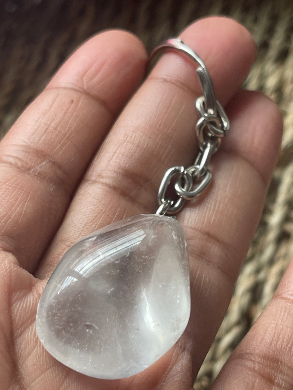 Clear teardrop-shaped crystal keychain a silver chain held in a hand.