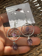 Dream Catcher Earrings, Silver dreamcatcher earrings with purple stones held in a hand against a woven background.