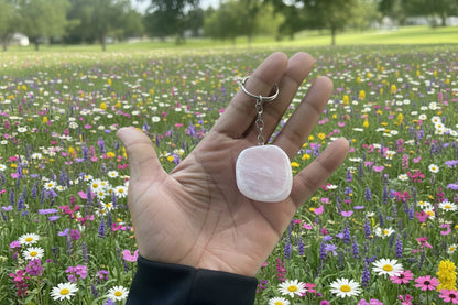 Hand holding a pink stone Ema Egg Seer Stone Polished Keychain with a keychain, blurred green background