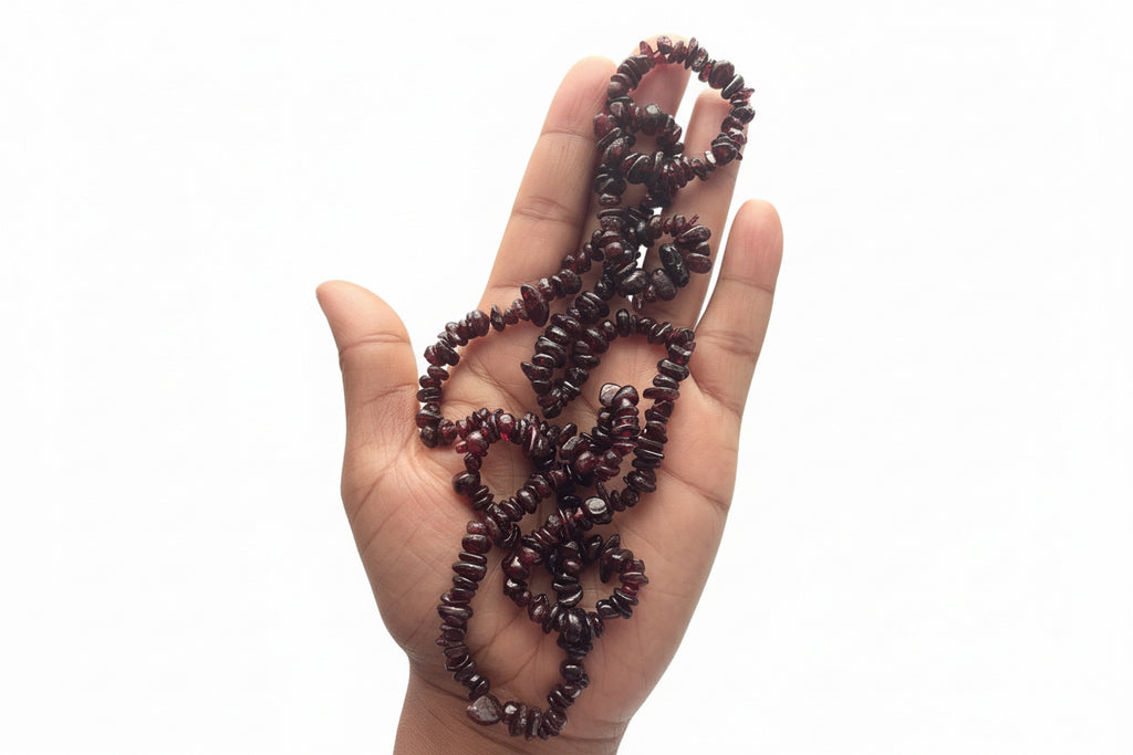 Hand holding a set of dark red beaded necklace known as Garnet stones on a white background 