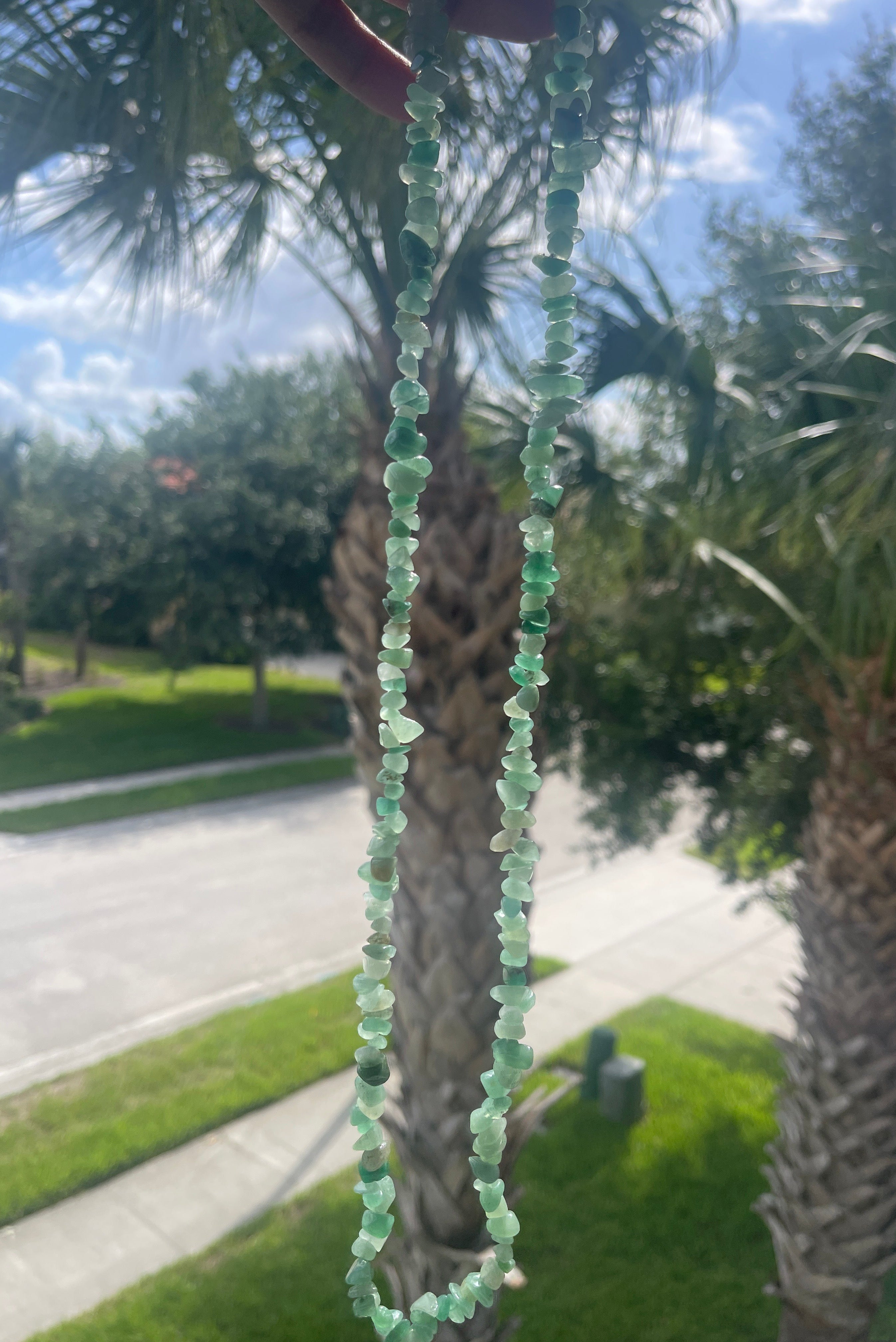 Green Aventurine chip beaded necklace against a palm tree and outdoor background 