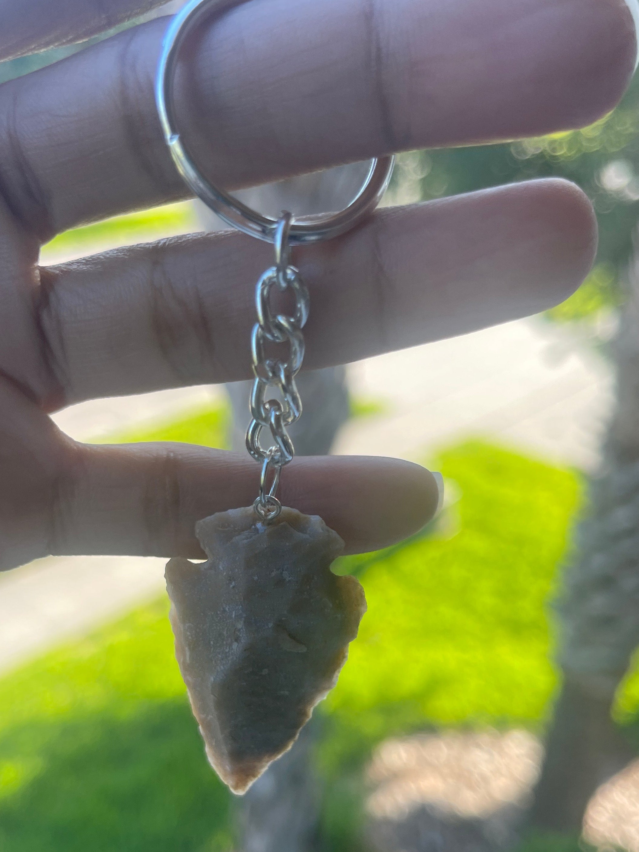 Hand holding a small arrowhead stone with a chain against a blurred natural background