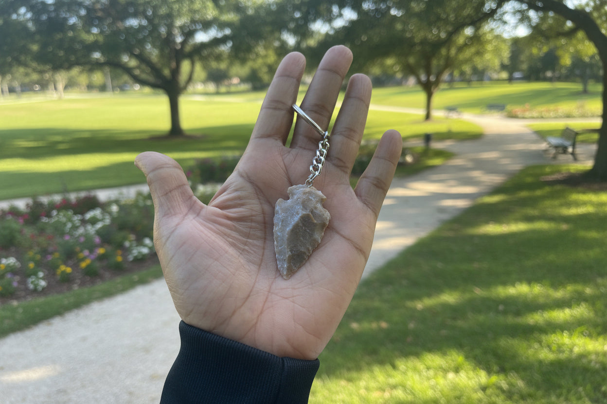 Hand holding a stone arrowhead pendant with a blurred natural park background