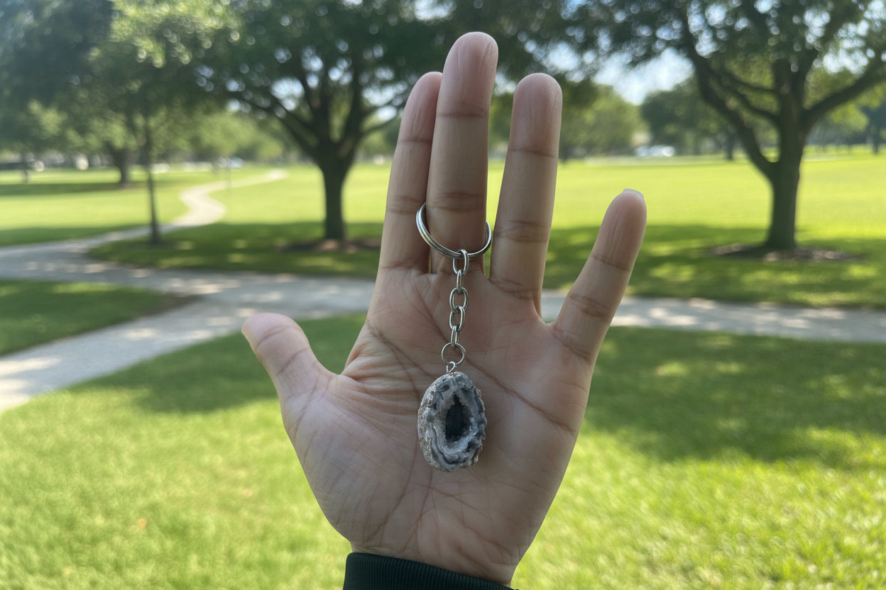 Hand holding a geode keychain with a stone-like object against a blurred outdoor background