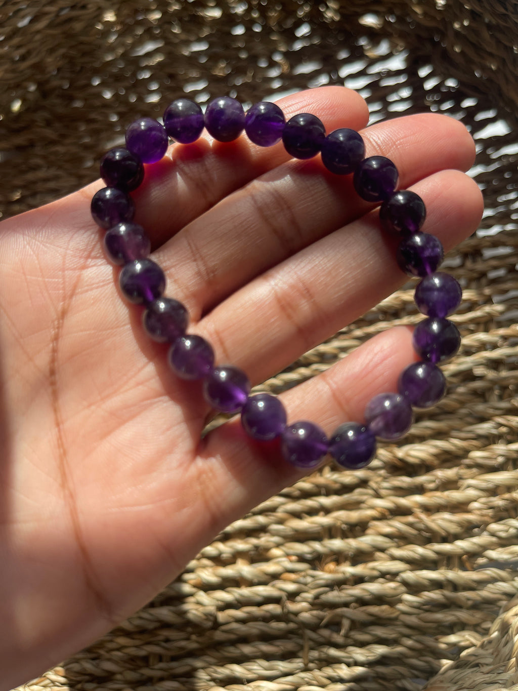 Hand holding a purple beaded bracelet against a woven background