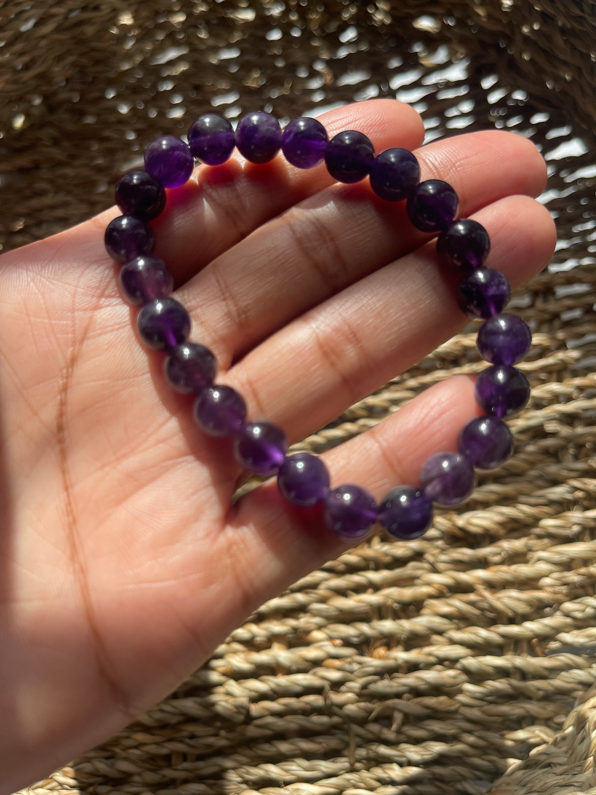Hand holding a purple beaded bracelet against a woven background