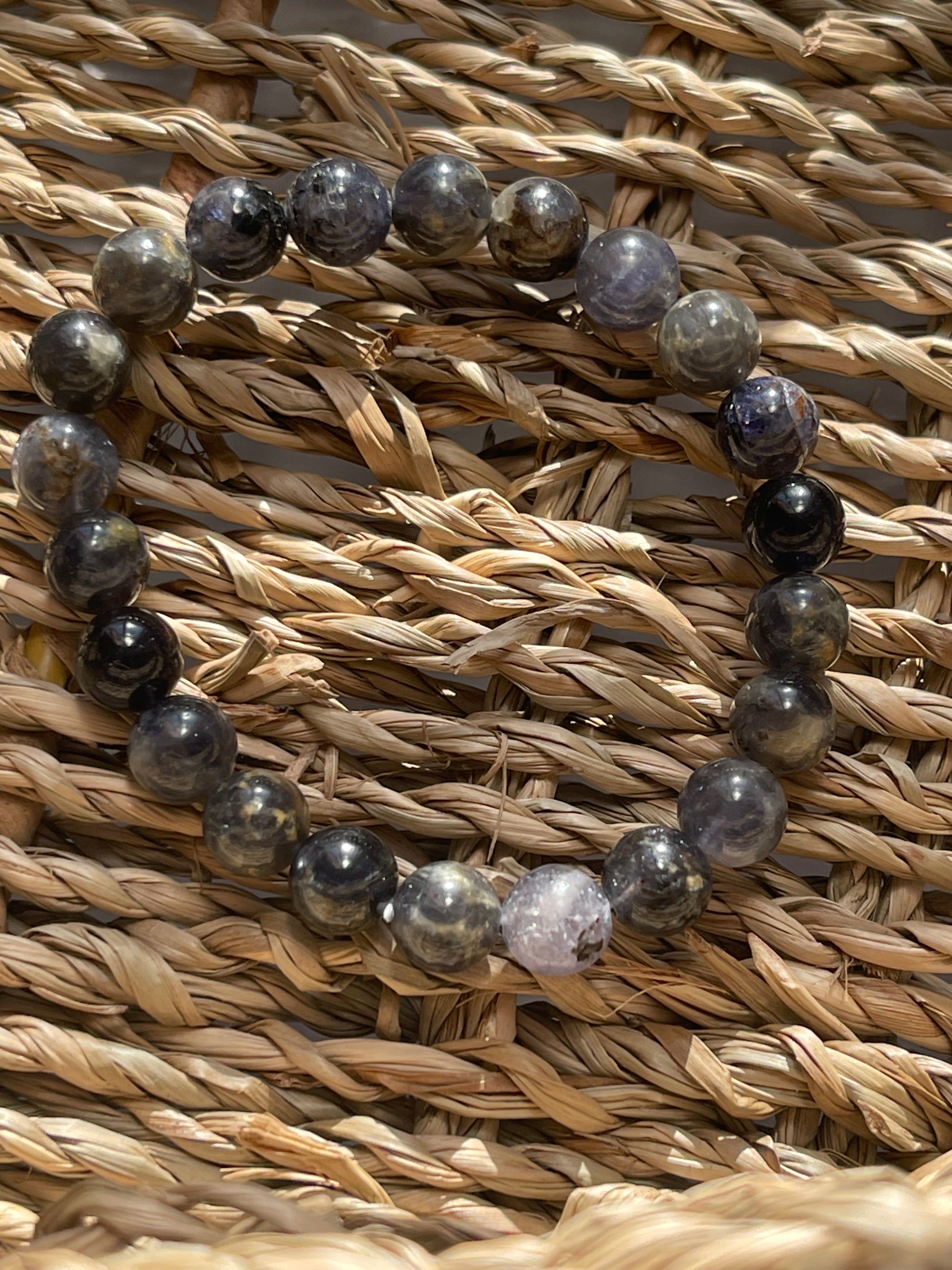 Iolite bracelet with dark beads on a woven straw background