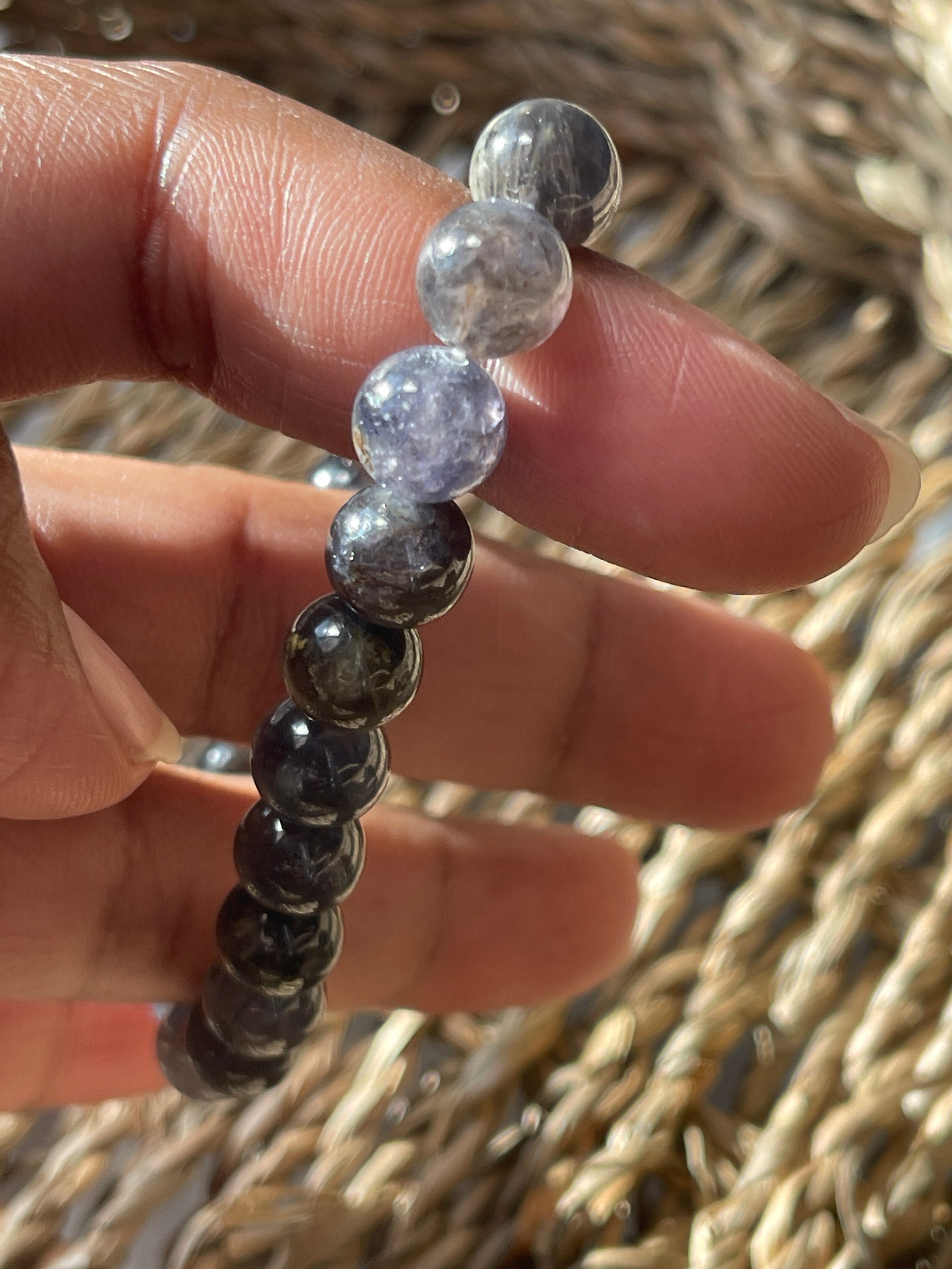 Hand holding a Iolite bracelet with clear and dark beads against a textured  background