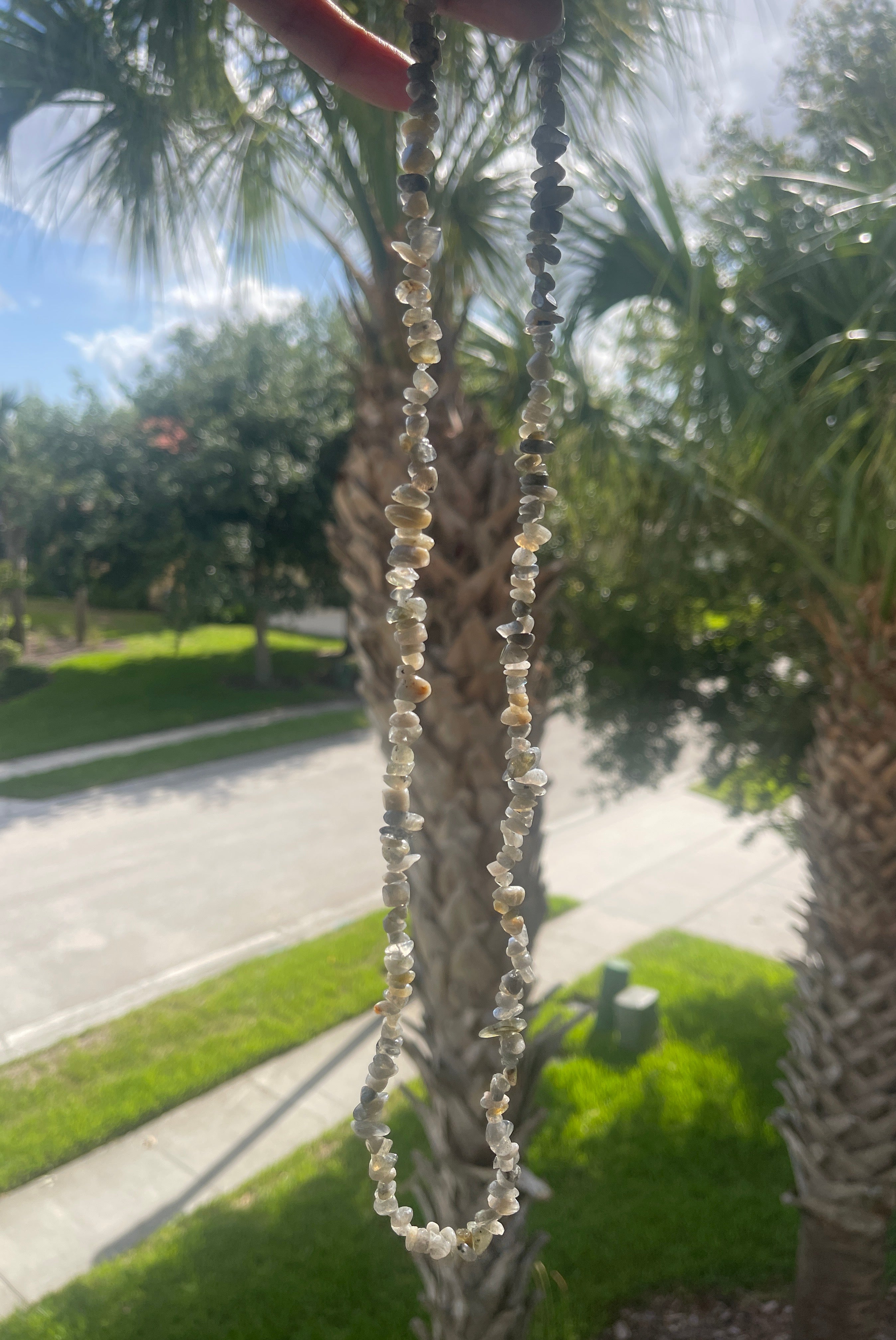 Labradorite_Chip_Necklace with clear stones held up against a blurred outdoor background
