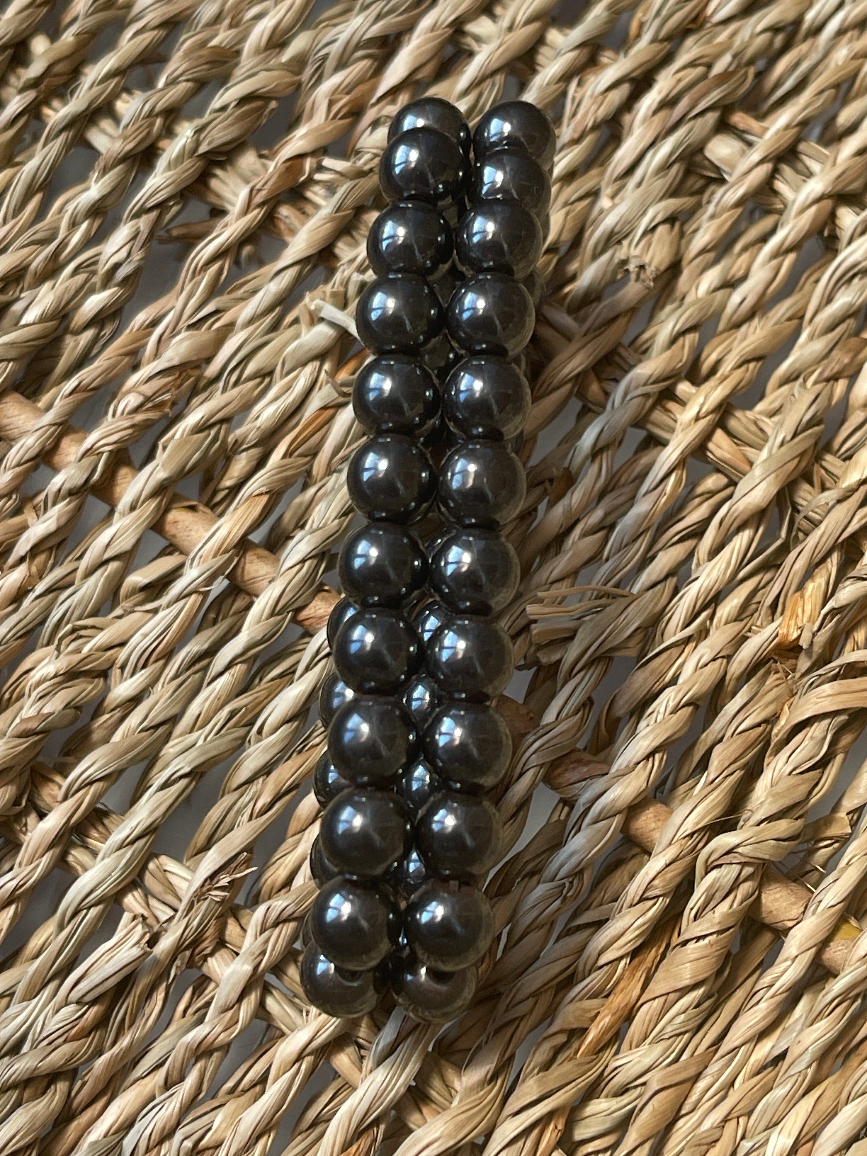 Magnetic Hematite Bracelet Row of black beads on a textured woven surface