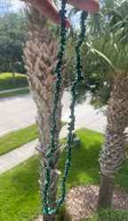 Person holding a Malachite_Necklace_30-32_Inches in front of palm tree branch