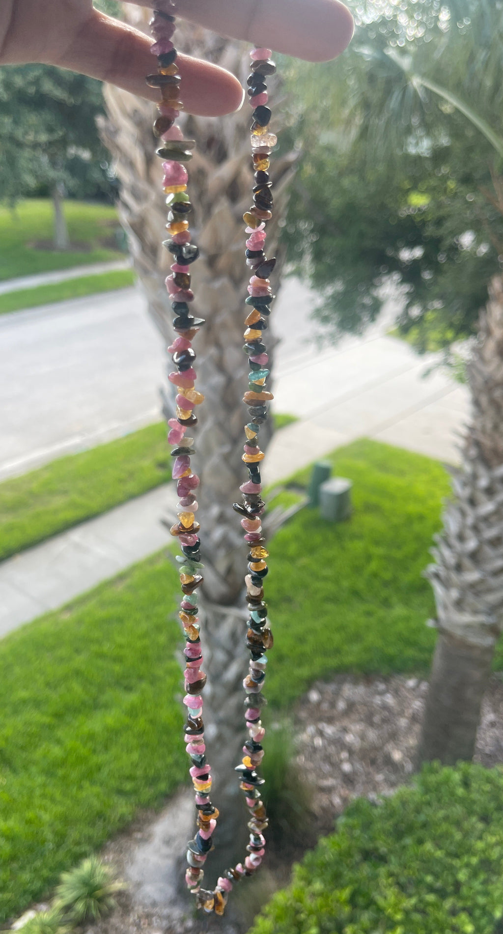 Colorful beaded Mixed_Color_Tourmaline_Necklace_30-32_Inches held up with a palm tree and grassy area in the background