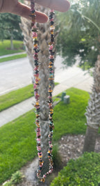 Colorful beaded Mixed_Color_Tourmaline_Necklace_30-32_Inches held up with a palm tree and grassy area in the background