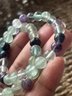 Close-up of a hand holding a beaded bracelet with clear and purple beads.