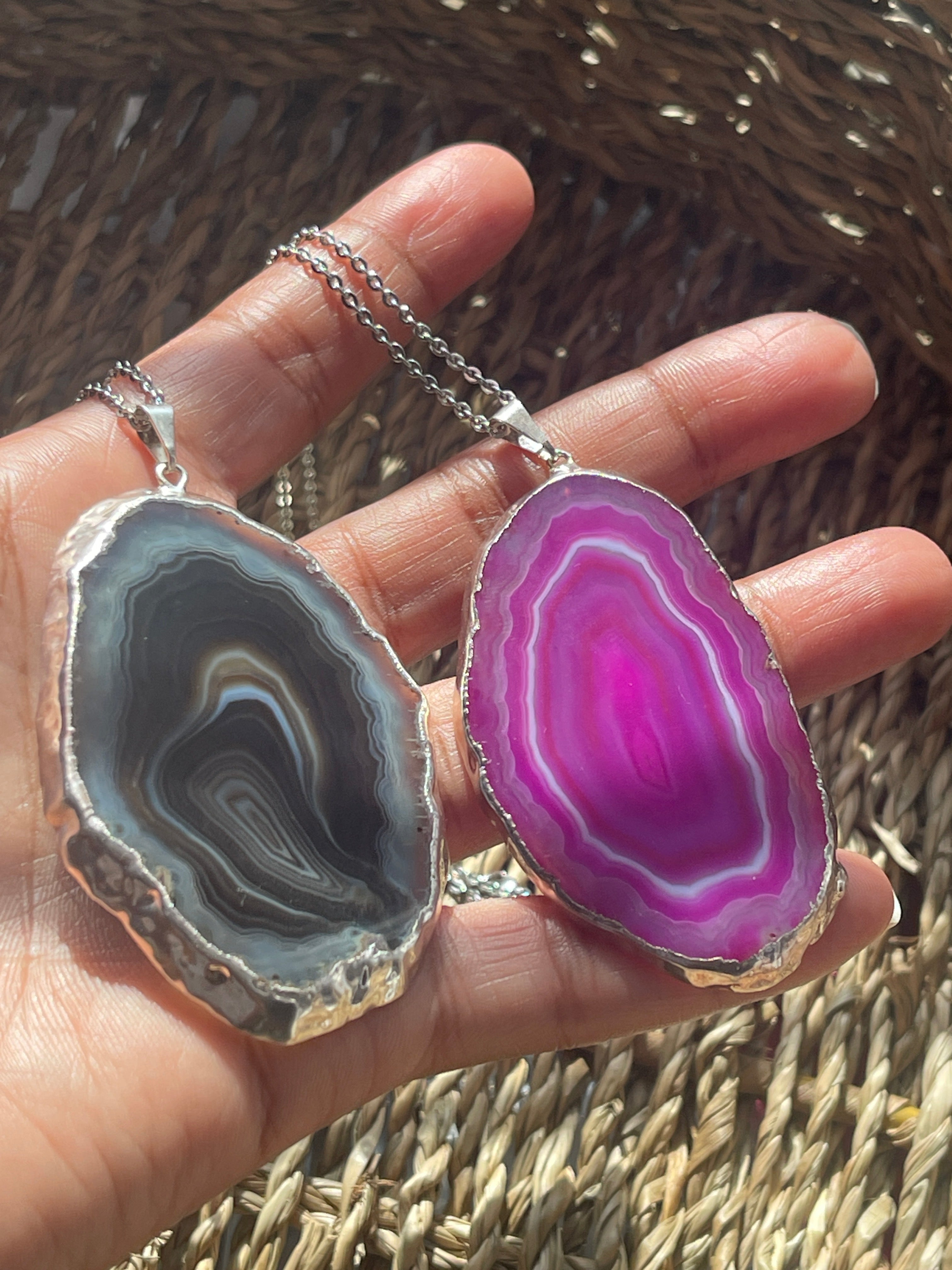 Hand holding a necklace with agate pendant against a woven background
