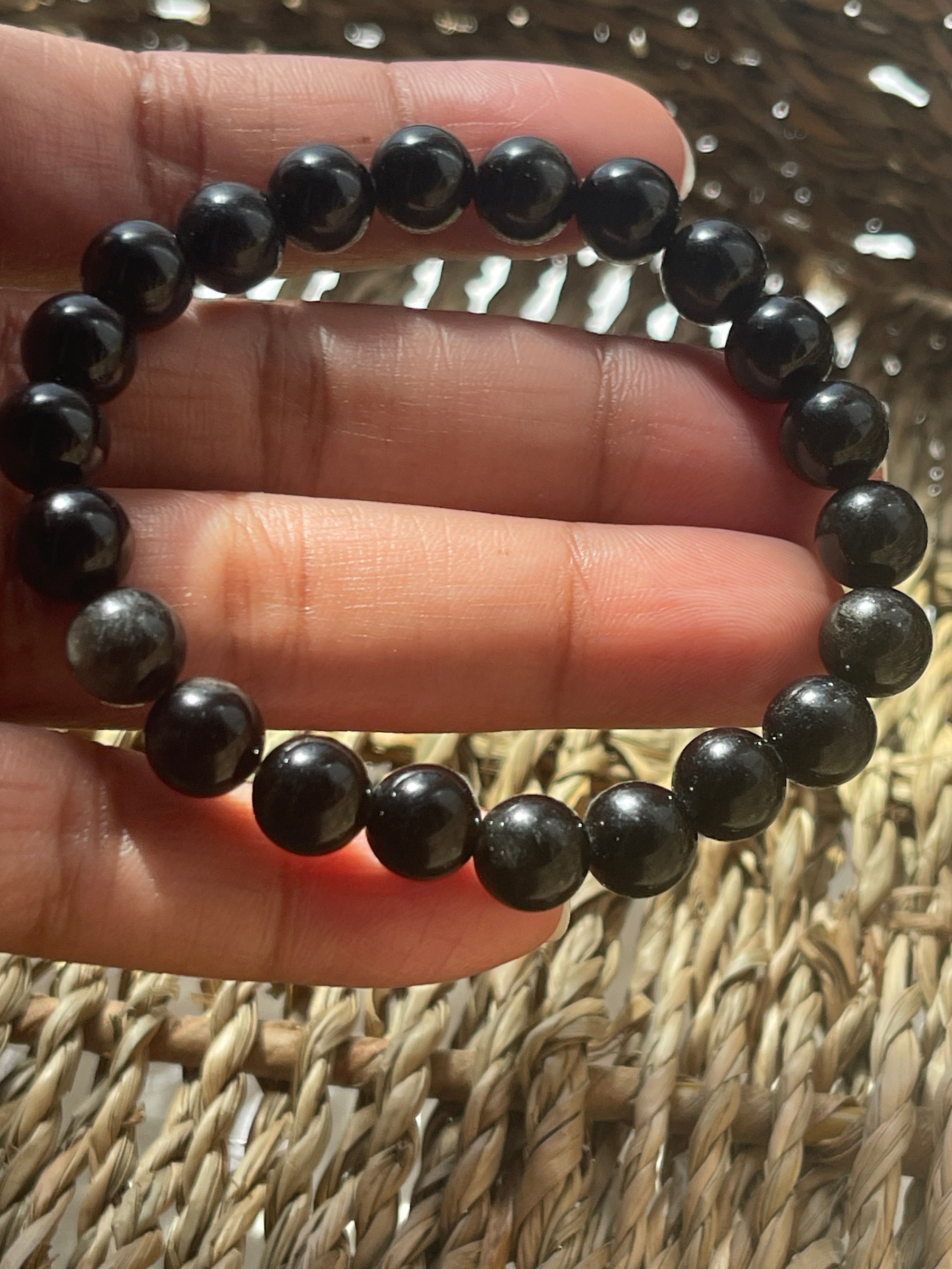 Black and gray beaded bracelet on a hand with a woven background