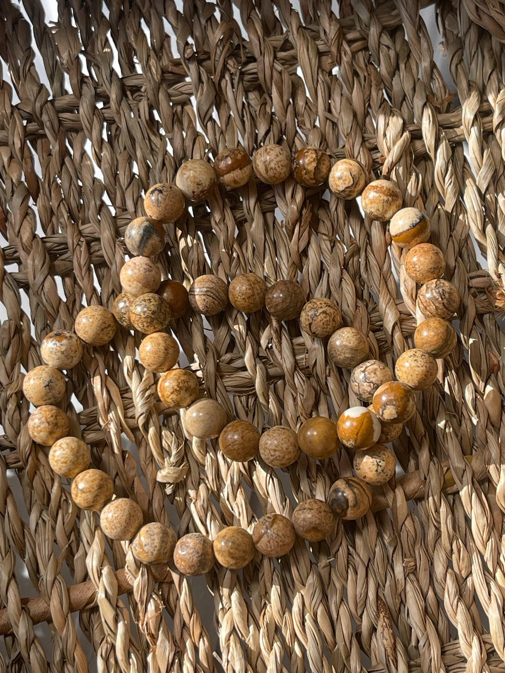 Picture Jasper beads arranged in a circular pattern on a woven surface