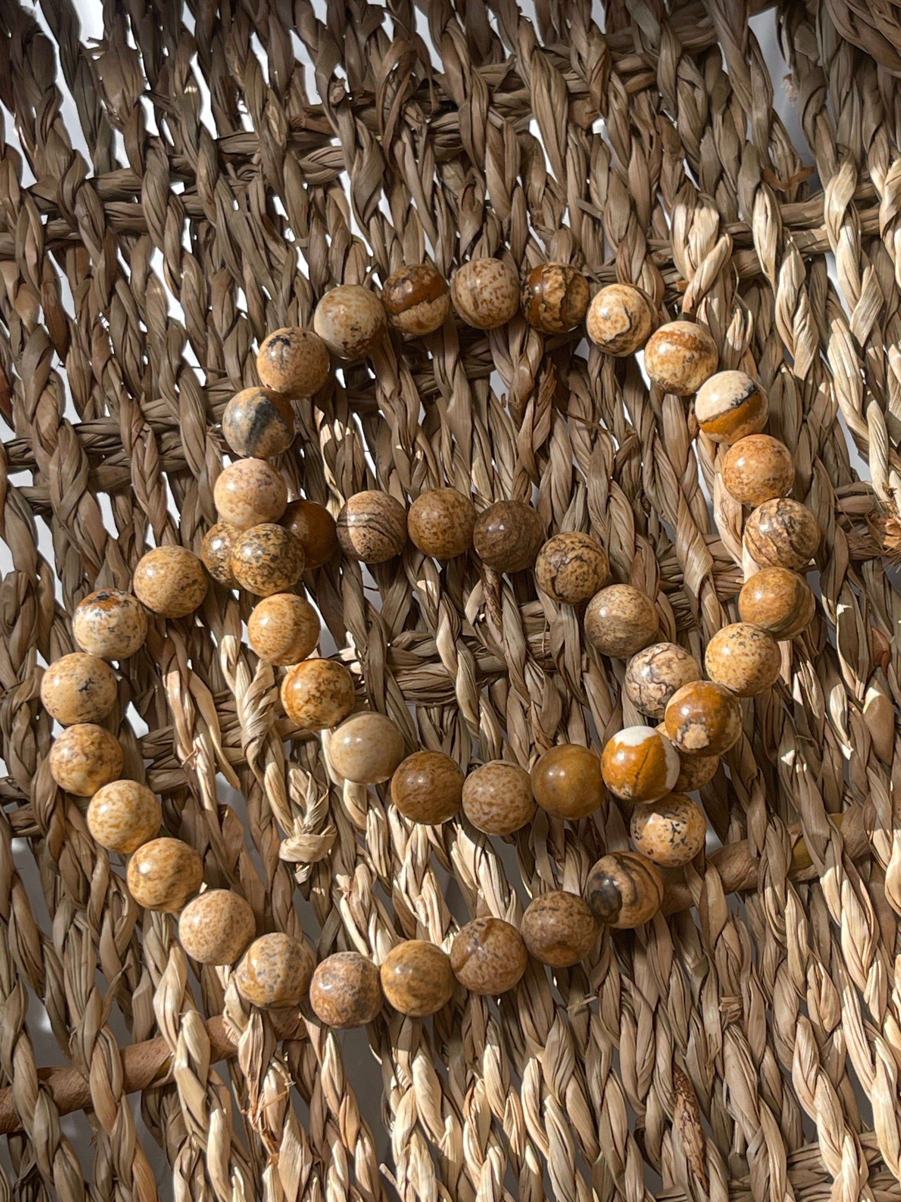 Picture Jasper beads arranged in a circular pattern on a woven surface