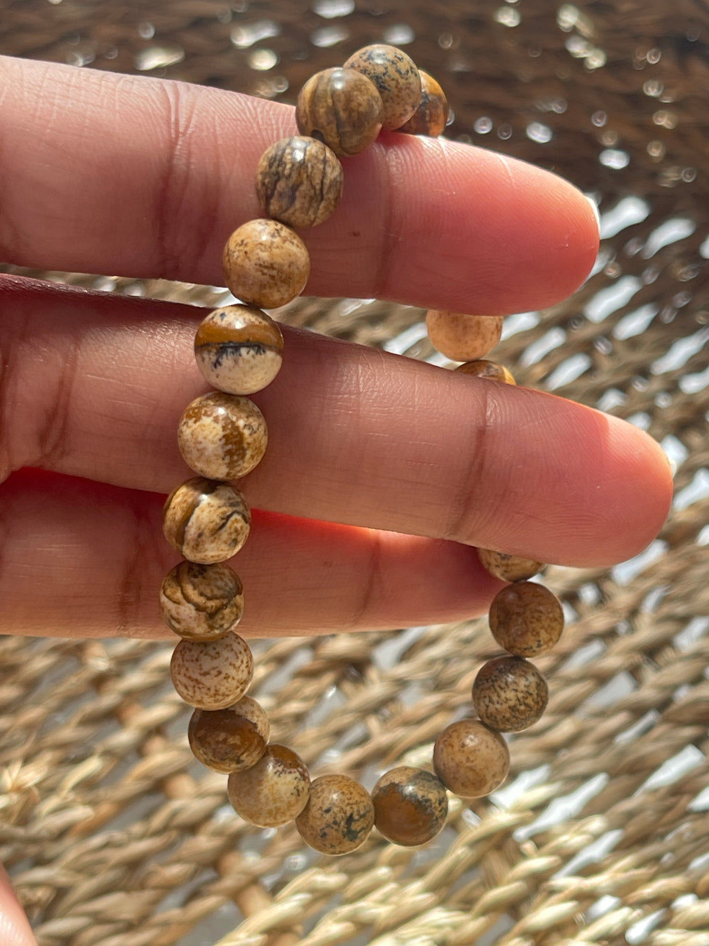 Hand wearing a beaded picture Jasper bracelet with a textured background