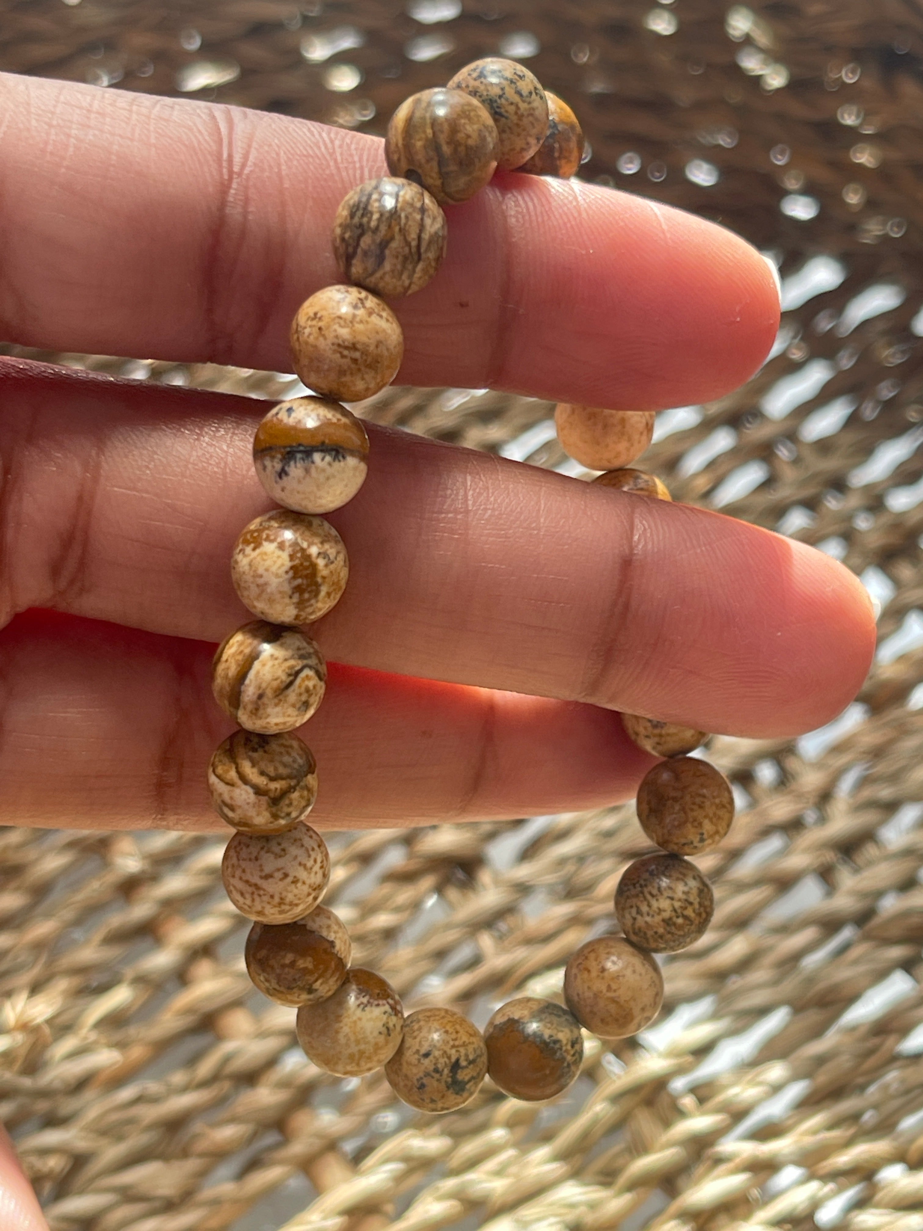 Hand wearing a beaded picture Jasper bracelet with a textured background