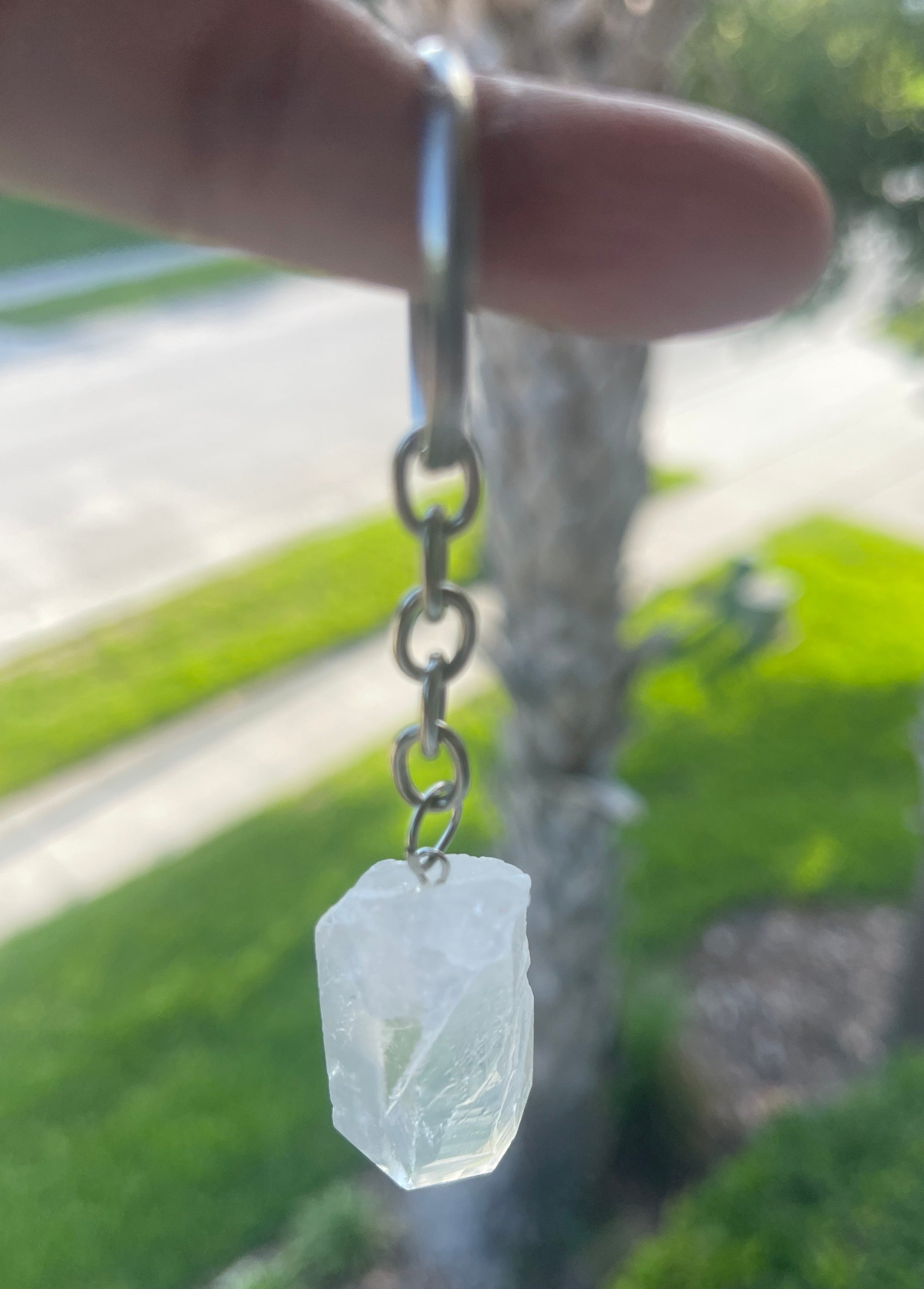 Crystal pendant on a chain held by a hand with a blurred green outdoor background