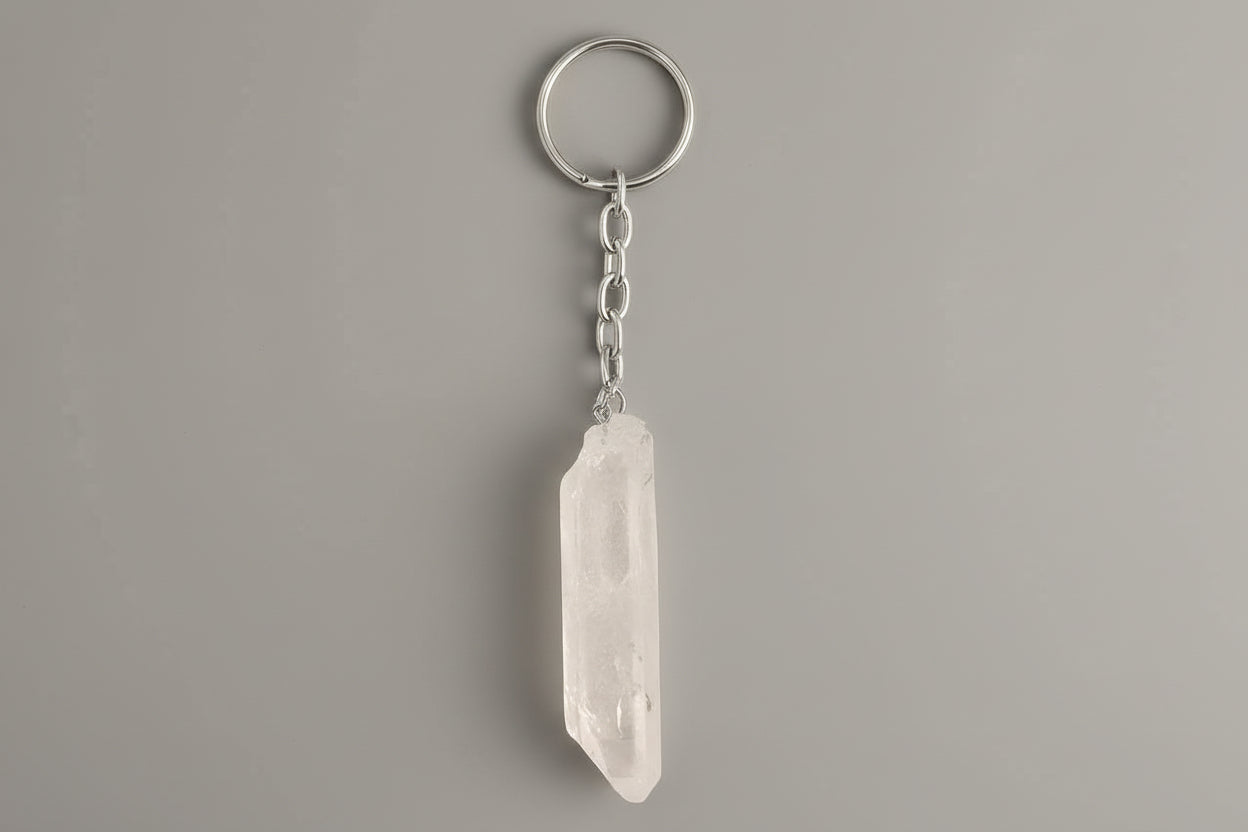 A clear quartz crystal point attached to a metal keychain ring, with the crystal hanging vertically against a gray background.