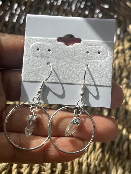 Quartz Point Circle Earrings, Clear crystal hoop earrings held by a hand with a branded card in the background.