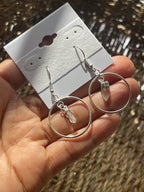 Quartz Point Circle Earrings, Silver hoop earrings held by a hand with a white card displaying more earrings in the background.