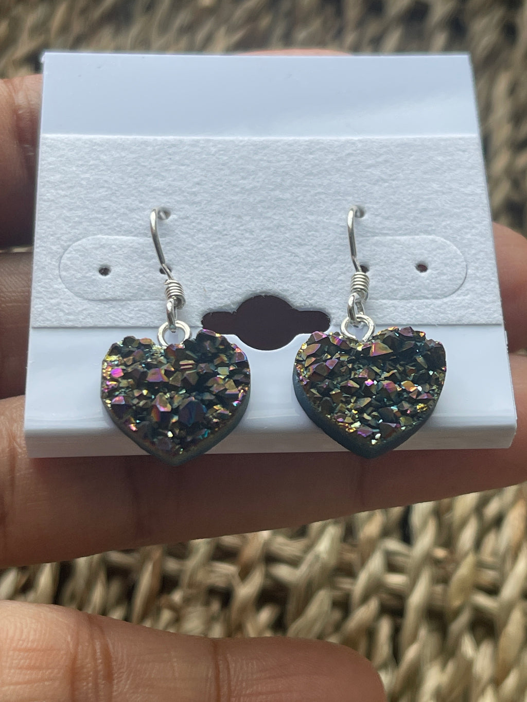 Rainbow Heart Coated Amethyst Earrings, Heart-shaped earrings with glittery finish on a white card held by a hand.