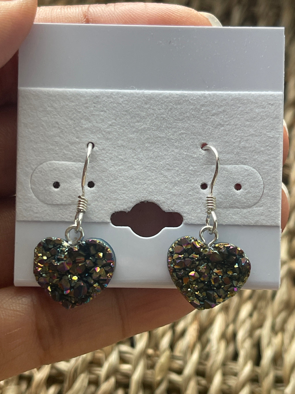 Rainbow Heart Coated Amethyst Earrings, Heart-shaped earrings on a white card held by a hand with a wicker background