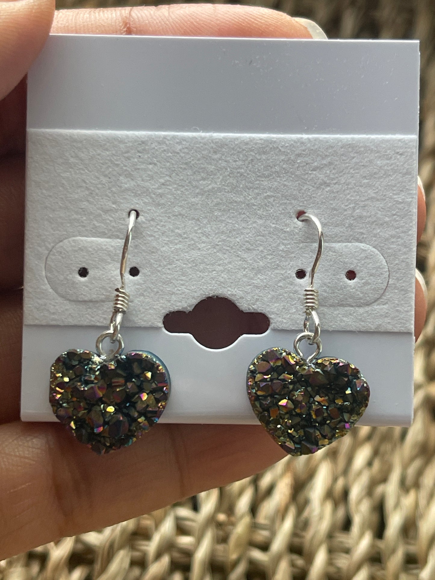 Rainbow Heart Coated Amethyst Earrings, Heart-shaped earrings on a white card held by a hand with a wicker background