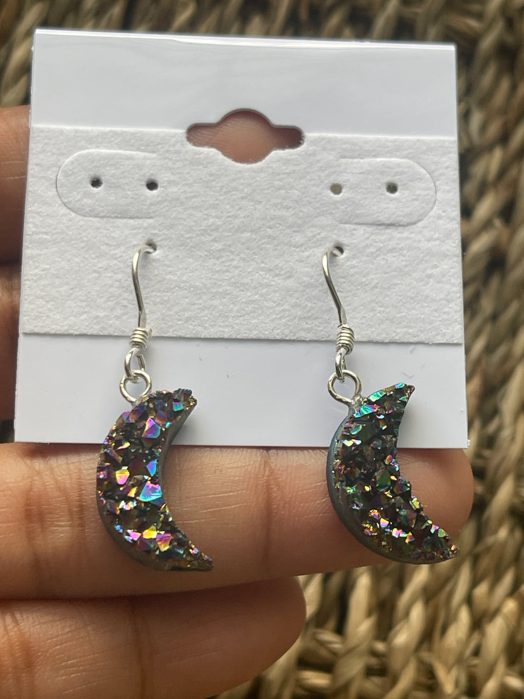 Rainbow Moon Amethyst Coated Earrings, Glittery crescent moon earrings held against a white card with a textured background.