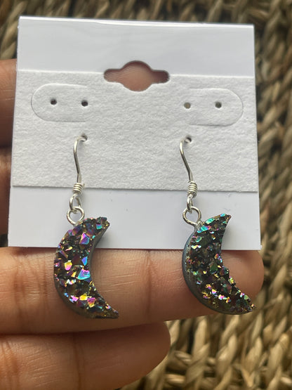 Rainbow Moon Amethyst Coated Earrings, Glittery crescent moon earrings held against a white card with a textured background.