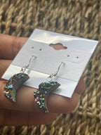 Rainbow Moon Amethyst Coated Earrings, Multicolored glittery earrings held by a hand against a textured background