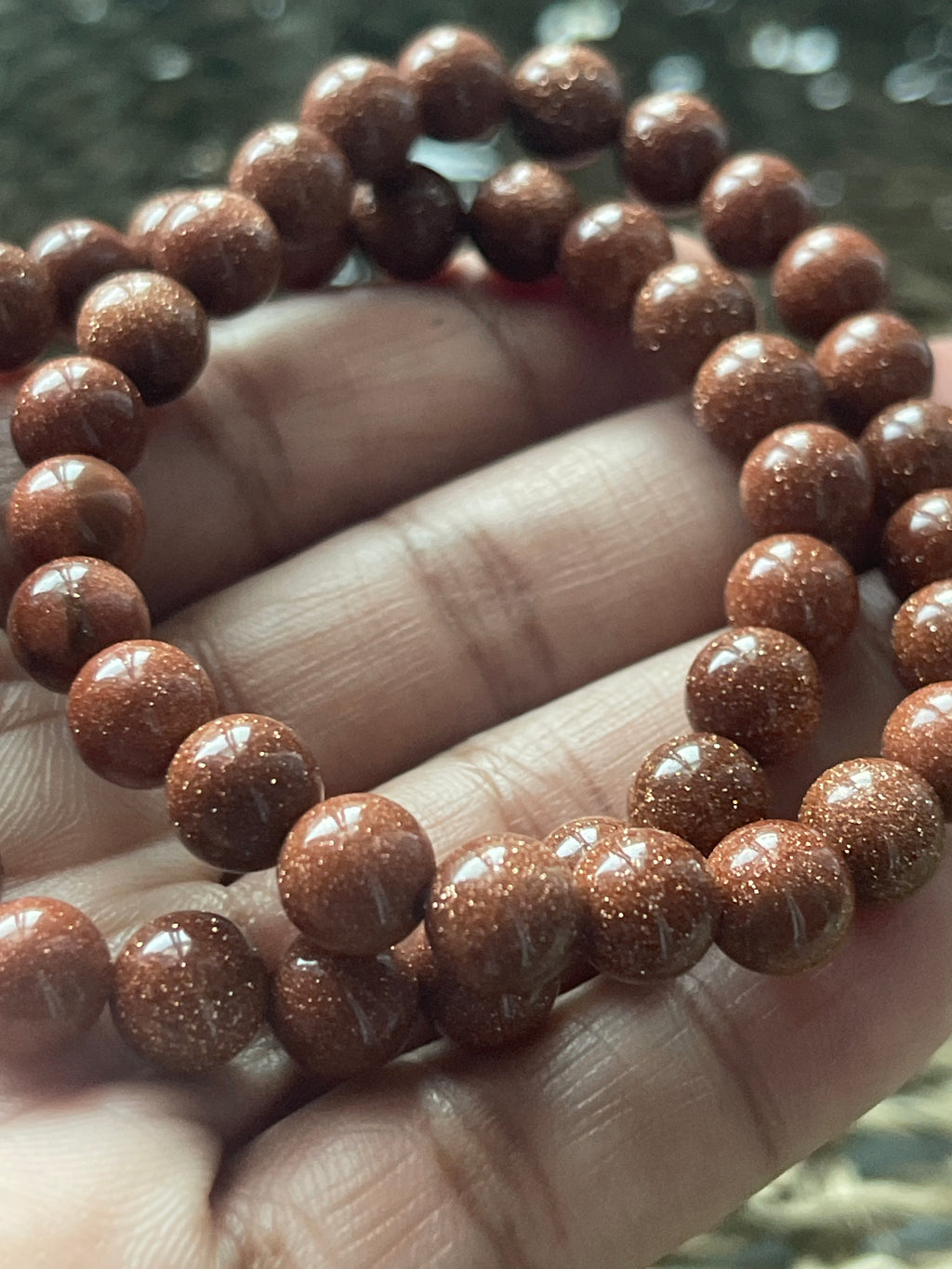 Close-up of a hand holding a red beaded bracelet against a blurred natural background