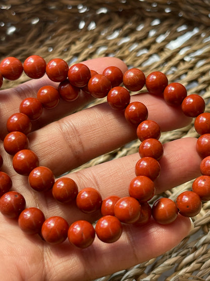 Close-up of a hand holding a string of red beads against a woven background