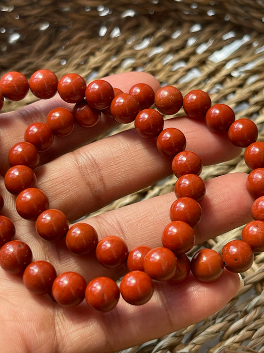 Close-up of a hand holding a string of red beads against a woven background