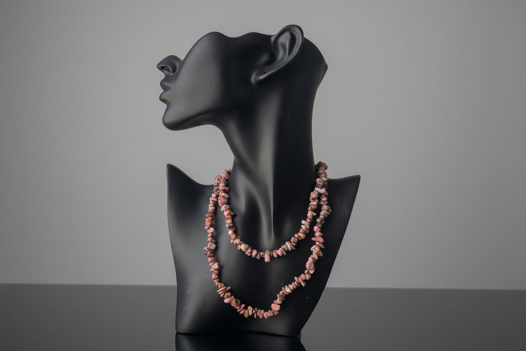 Black mannequin head with a pink Rhodonite beaded necklace on a neutral background