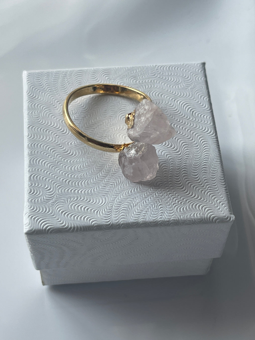 Rose quartz gold ring with pink crystals on a textured white jewelry box