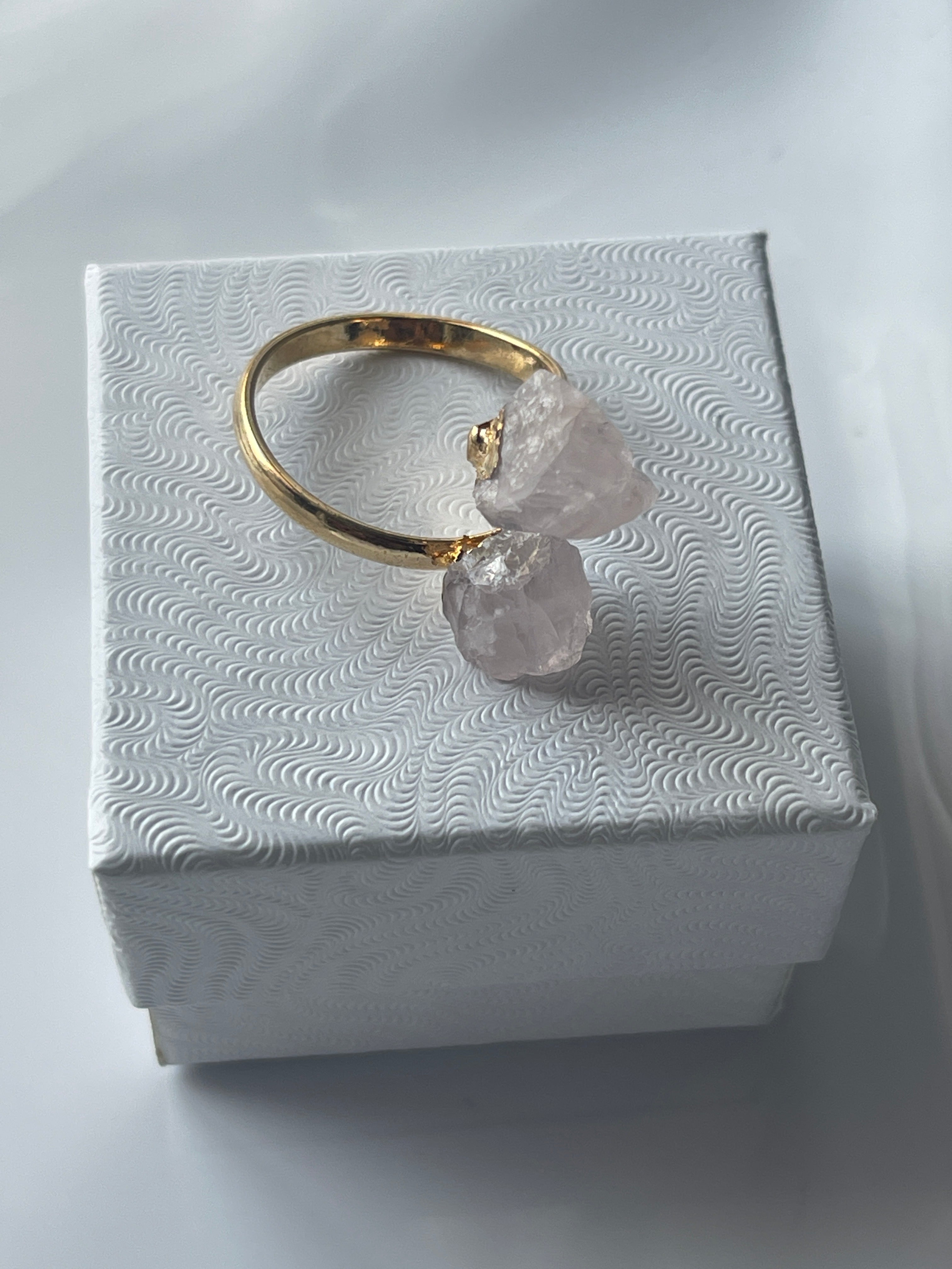 Rose quartz gold ring with pink crystals on a textured white jewelry box