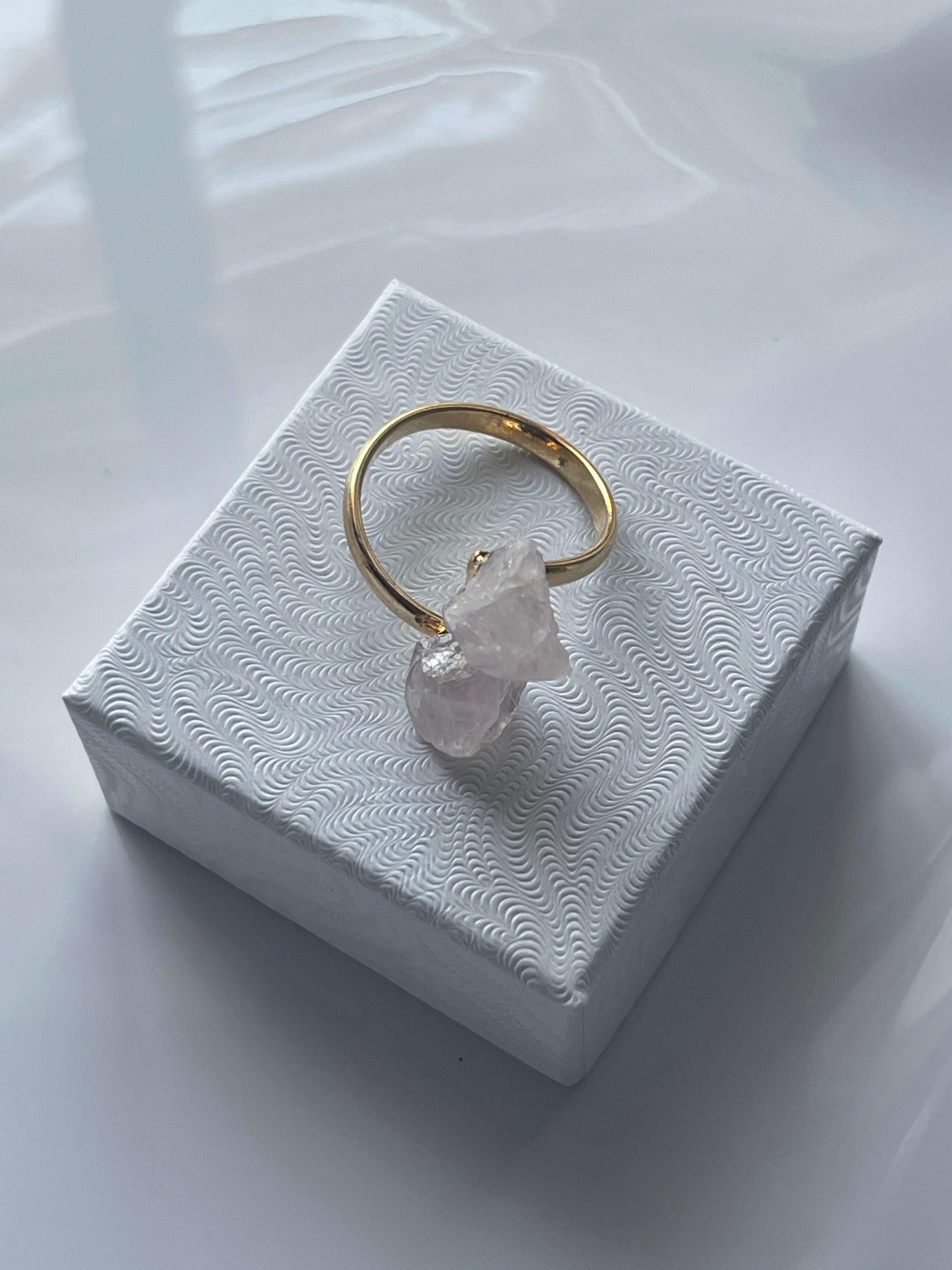 Rose quartz gold ring with a pink crystal on a textured white jewelry box