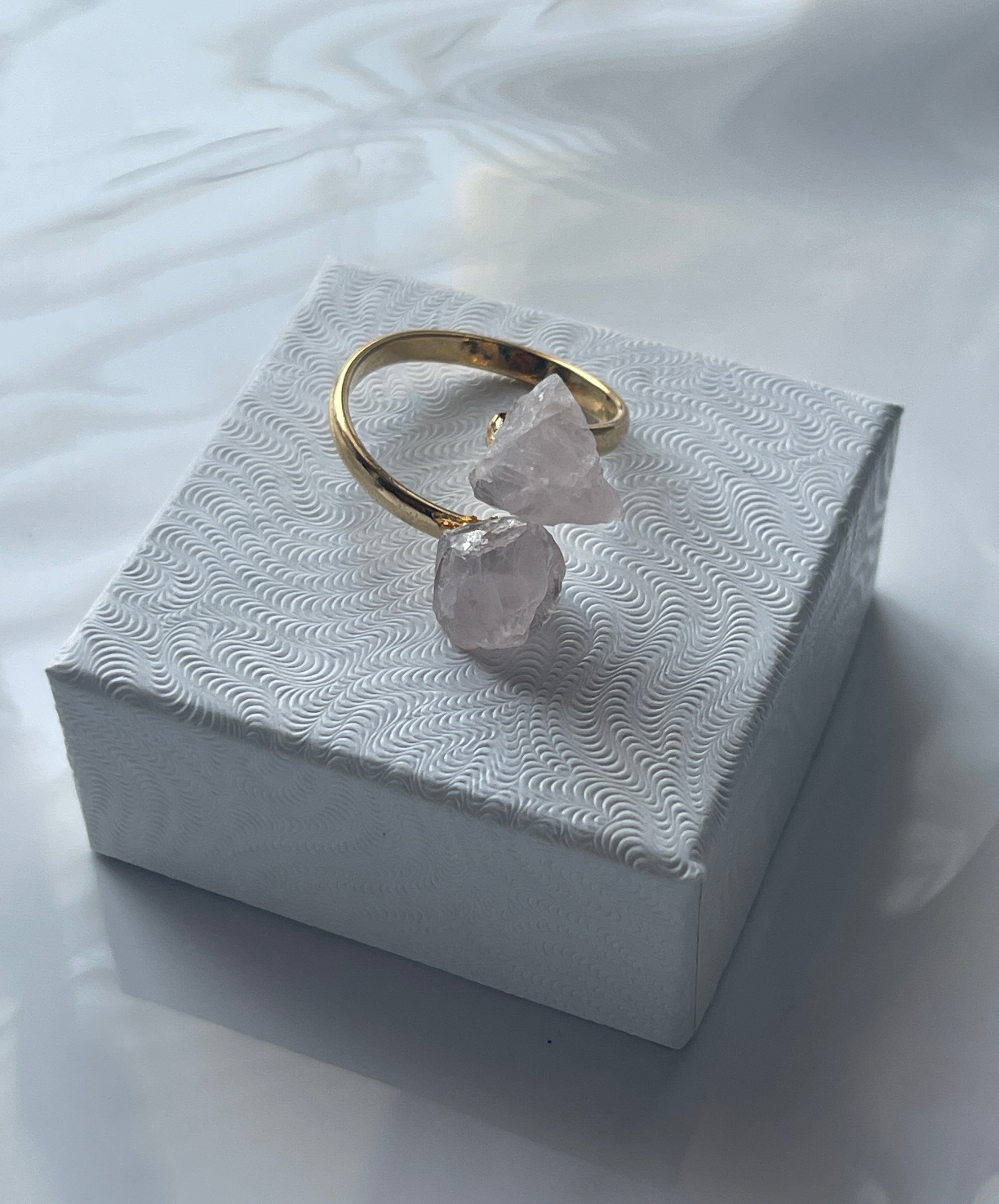 Rose quartz gold ring with a pink crystal on a textured white jewelry box top 