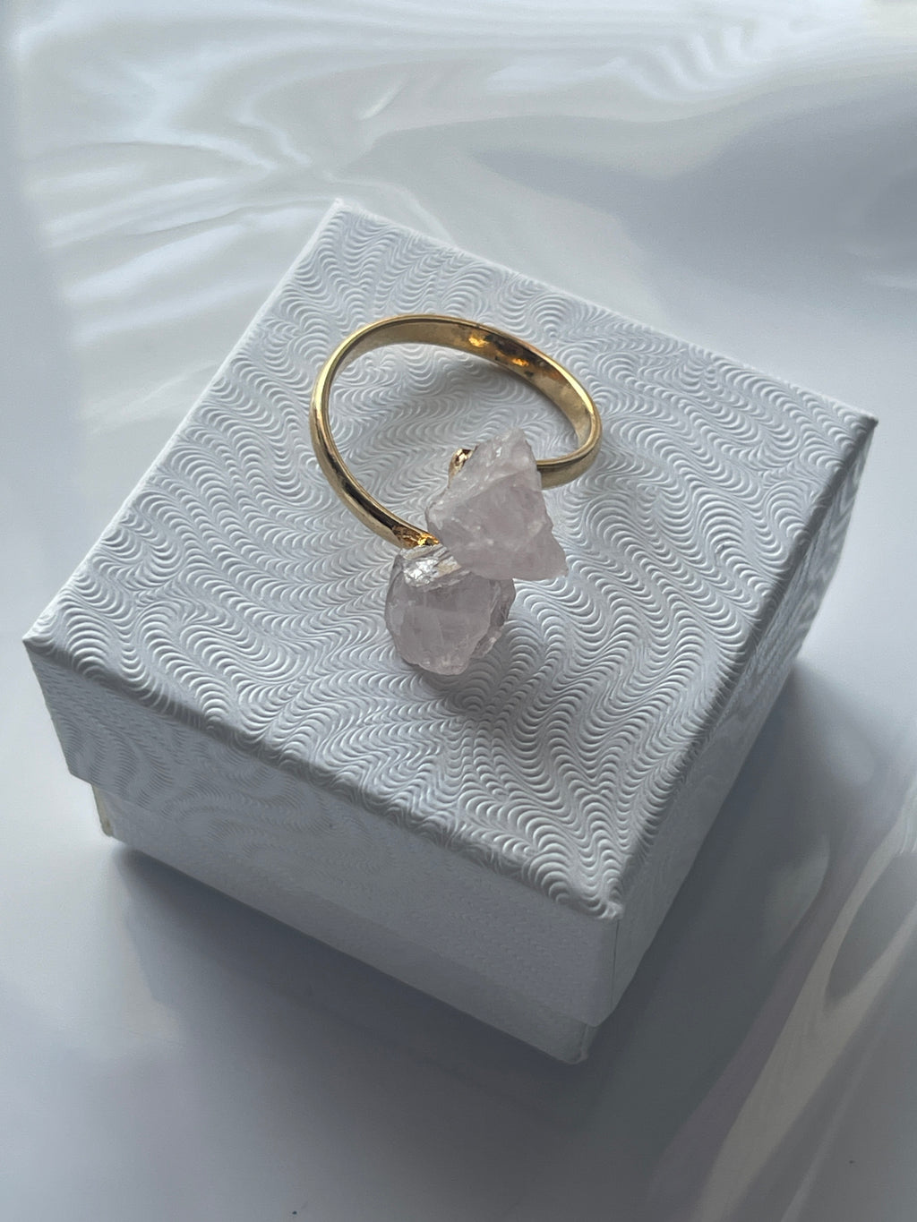 Rose quartz gold ring with a pink crystal on a textured white jewelry box