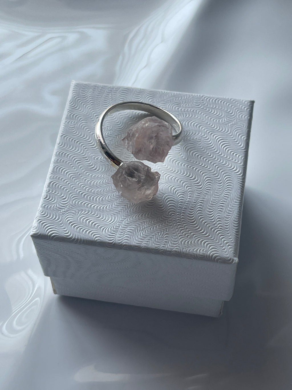 Rose quartz sliver ring on a textured white jewelry box 