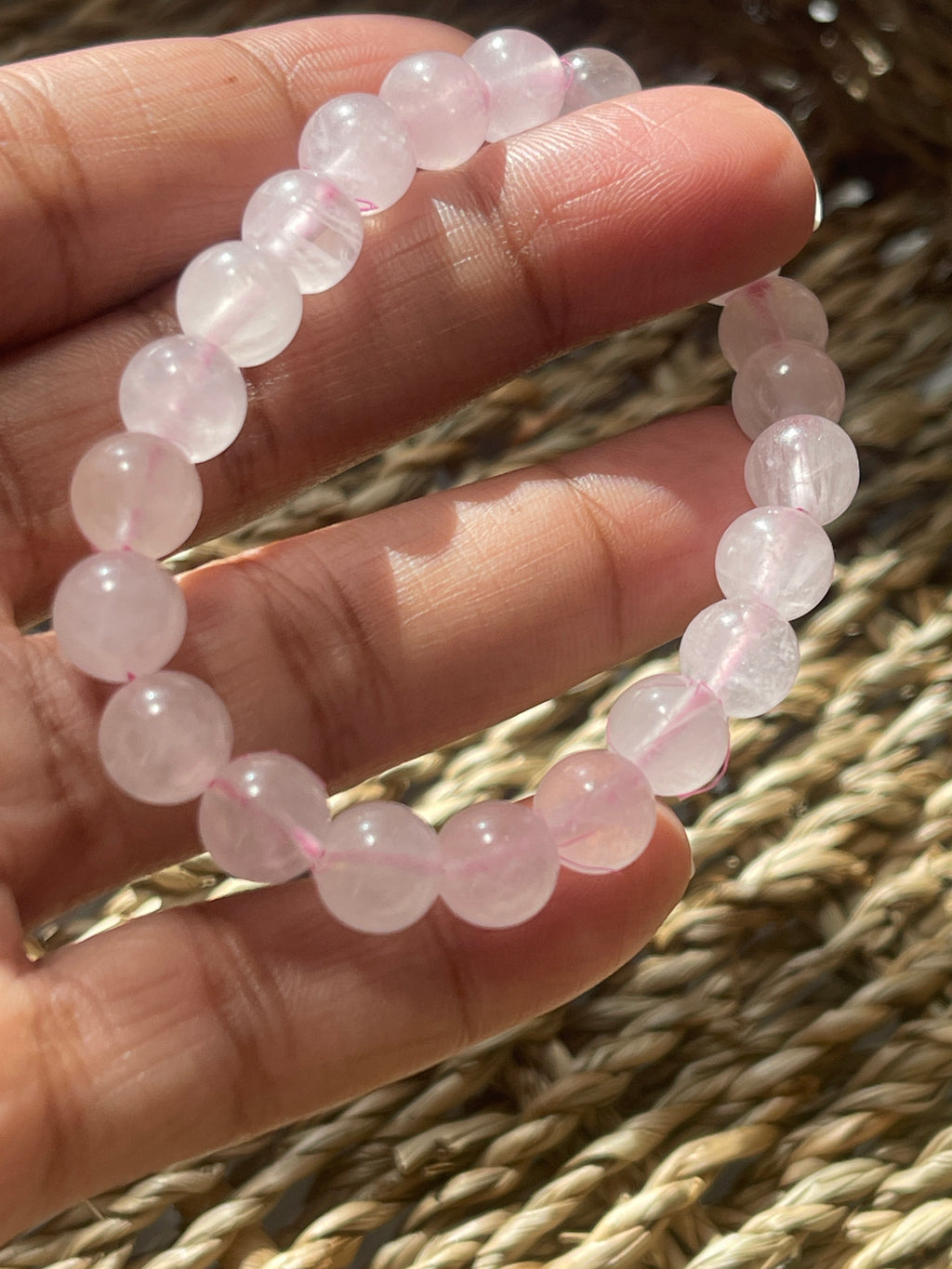 Hand holding a pink quartz bracelet with pink beads against a woven background