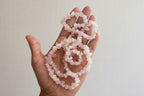 Hand holding a set of pink beaded rose quartz necklace against a plain white background